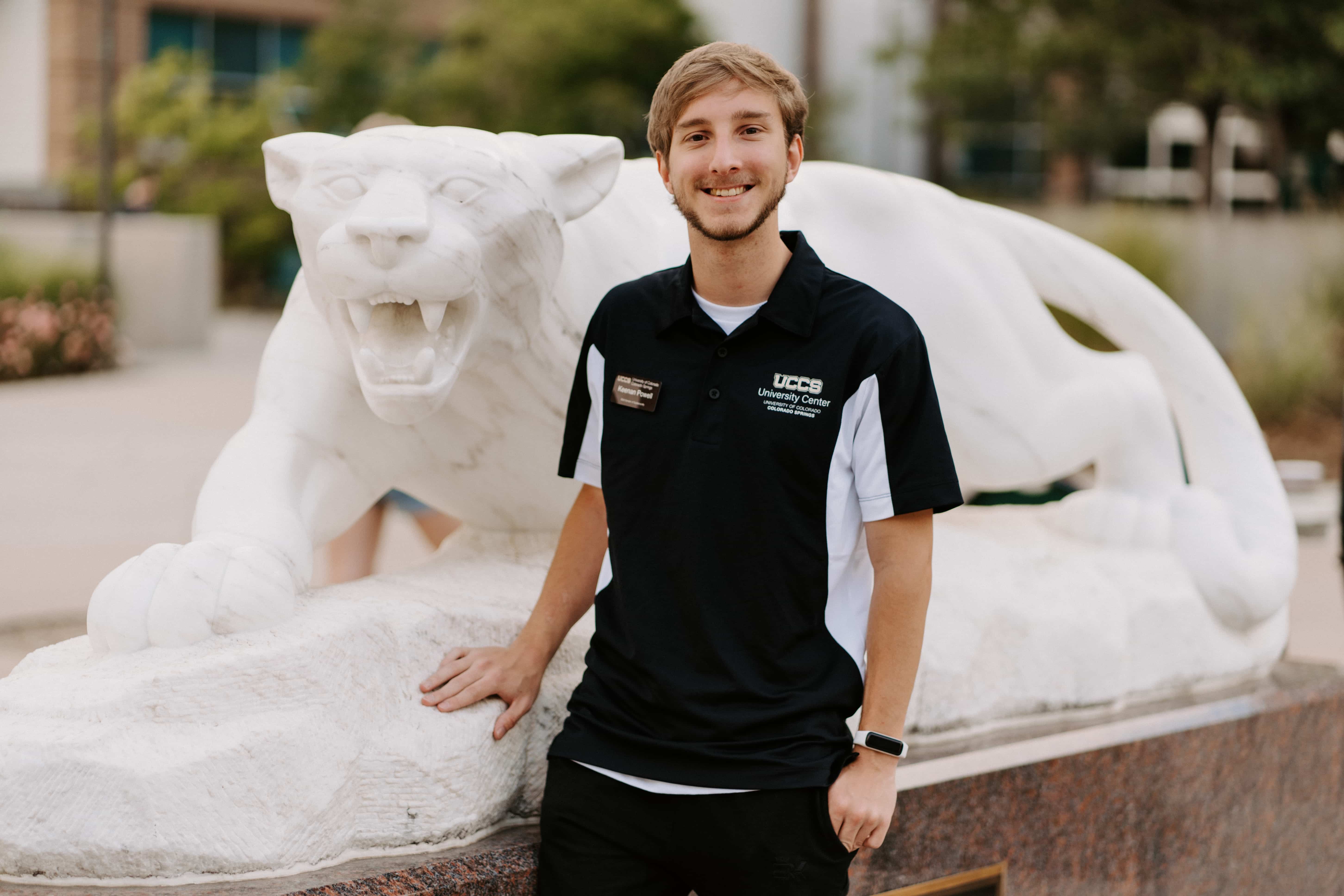 Image of Keenan Powell in a dark polo in front of a mountain lion statue