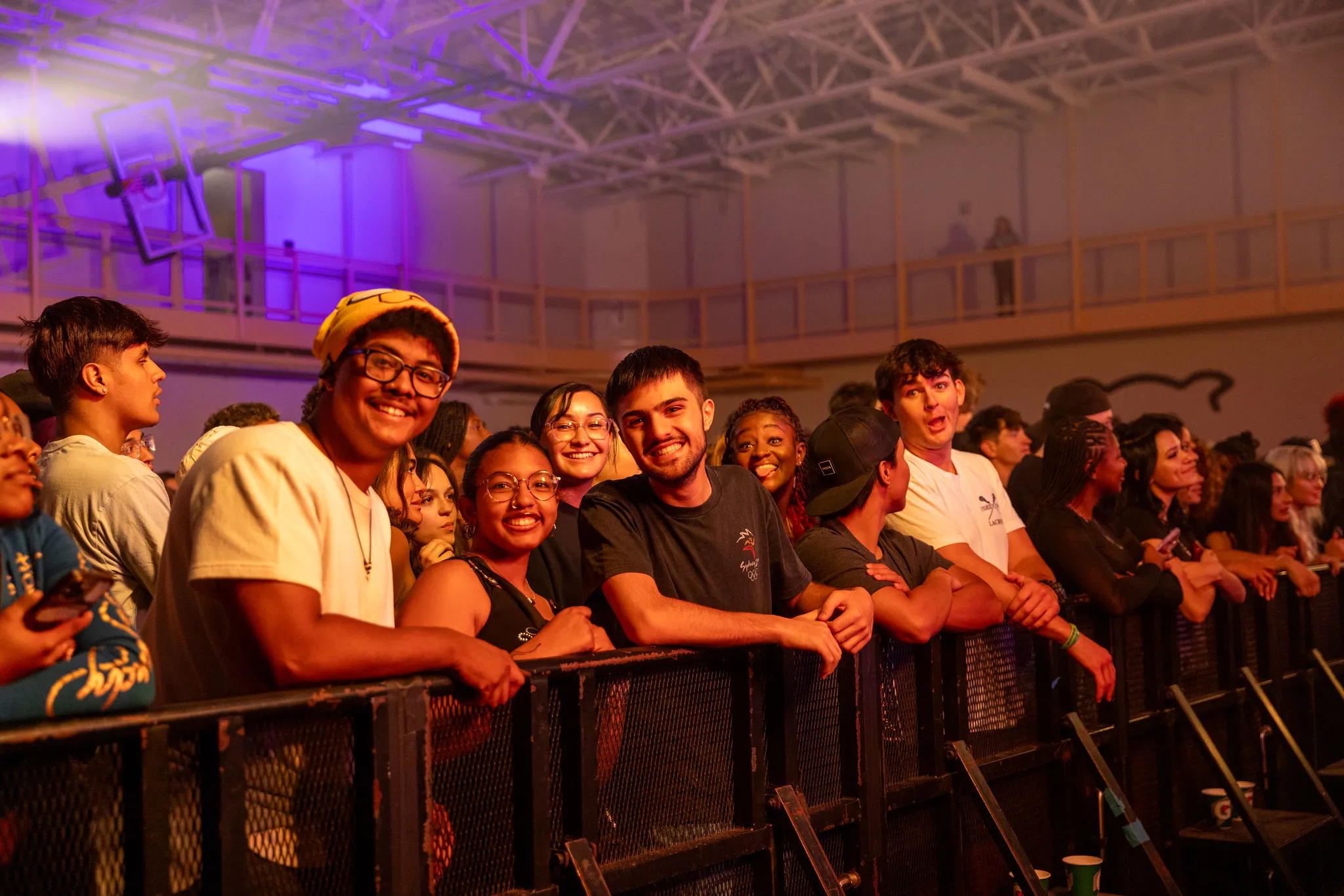 Students leaning on the crowd control barriers in yellow lighting at a concert.