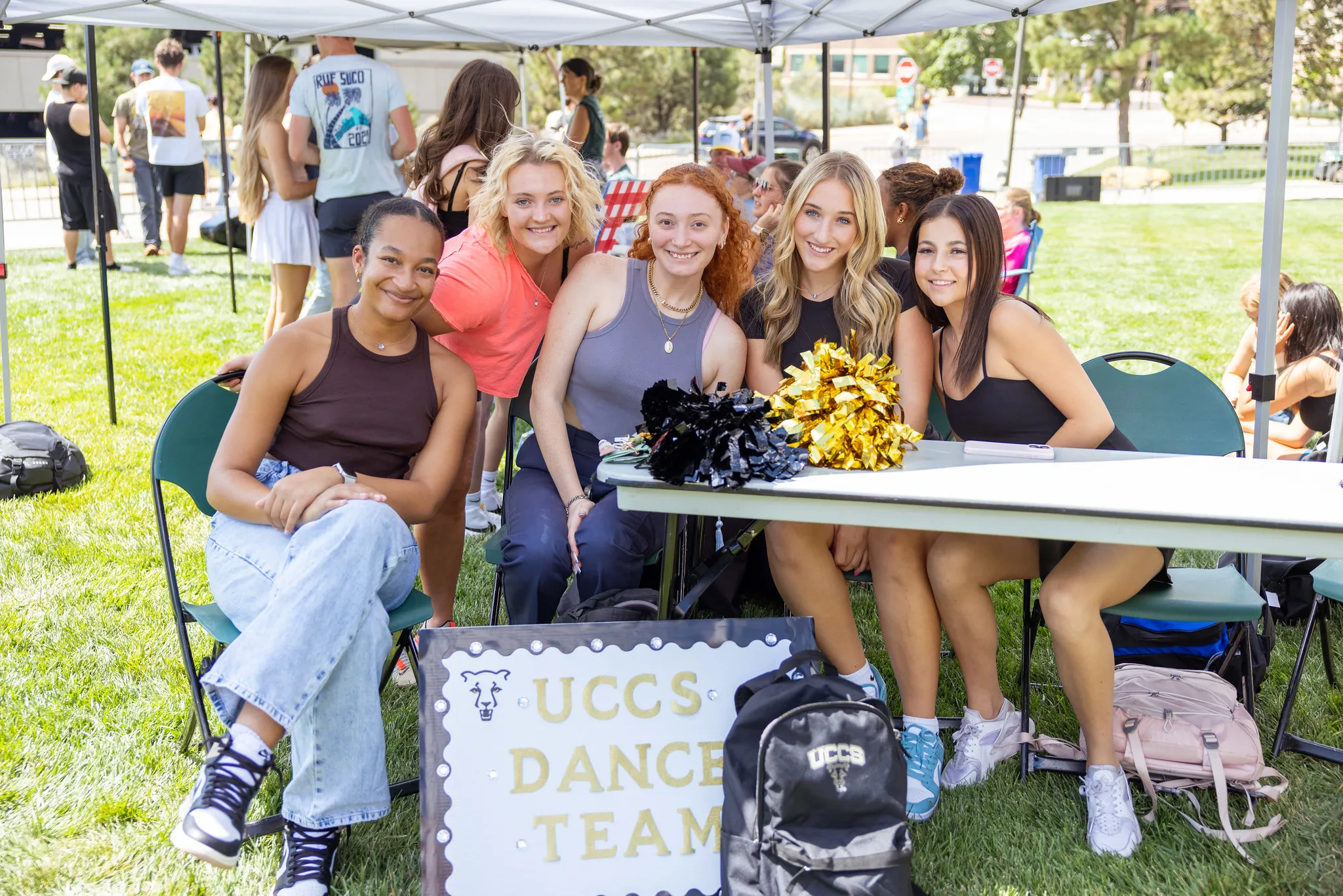 A group of people smiling at the camera with a "UCCS Dance Team" sign at a club fair.